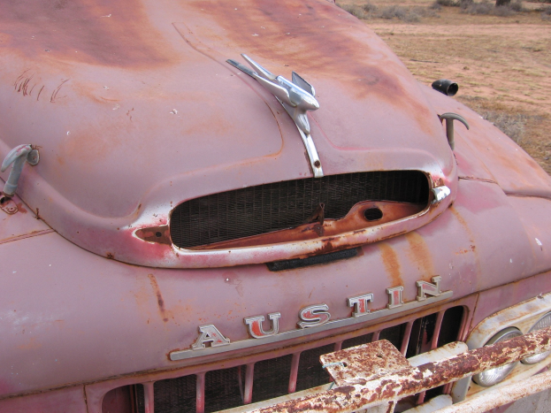 Alter rostiger Lkw auf einem Feld mit Bäumen und einem klaren blauen Himmel, von Rost bedeckt durch langfristige Exposition gegenüber den Elementen.