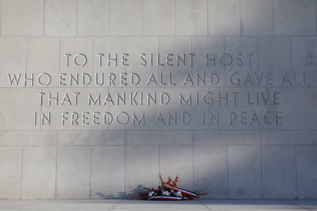 Eine Gedenkwand mit der Inschrift "Dem stillen Gast, der alles ertrug und alles gab, damit die Menschheit in Freiheit und Frieden leben könne.", geschmückt mit einem Blumenstrauß.