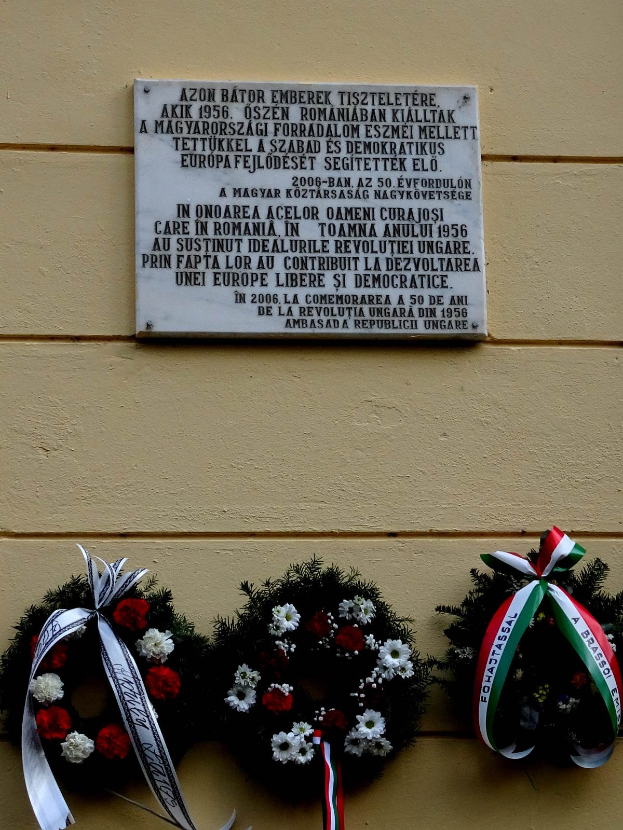 Zwei Kränze mit Bändern hängen an einem Gebäude neben einer Gedenktafel für Holocaust-Opfer.