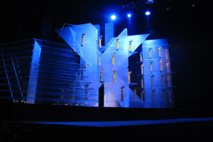 Bühne für eine Preisverleihung mit dunklem Hintergrund und wenigen Lichtern, mit Gegenständen, die wahrscheinlich mit dem Event zu tun haben.