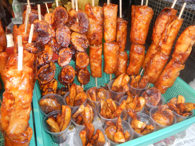 Ein grüner Tablett auf einem Tisch voller Hühnerspieße und verschiedenen anderen Speisen, mit Menschen und Flaschen im Hintergrund.