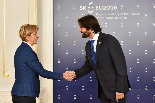 Bundeskanzlerin Angela Merkel und Joachim Gauck schütteln sich die Hände bei einem EU-Gipfeltreffen, lächeln und stehen vor einem Banner und einer Tür.
