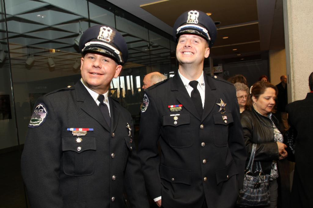 Zwei lächelnde Beamte im Vordergrund, Menschen in der Mitte, Glasfenster links, Lichter und Decke oben und Säulen und Menschen rechts.