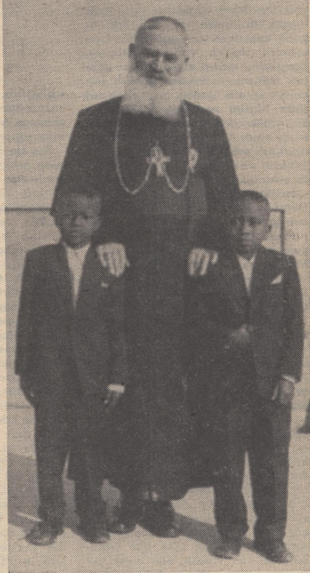 Ein Schwarz-Weiß-Foto eines Mannes, der neben zwei Jungen in Blazern und Krawatten steht, mit Text am unteren Rand, der darauf hindeutet, dass er ihr Vater ist.