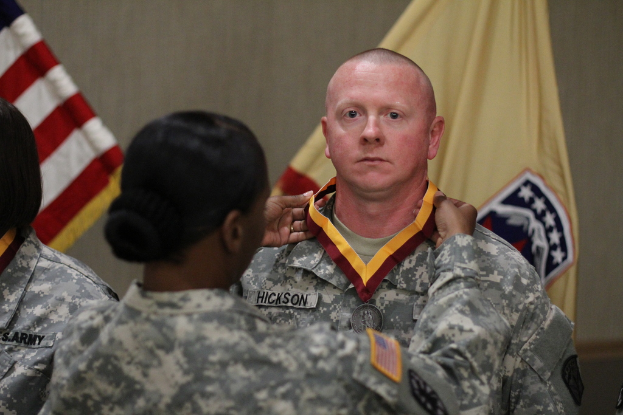 Eine Frau berührt die Medaille eines Mannes, der vor ihr steht, mit Flaggen im Hintergrund.