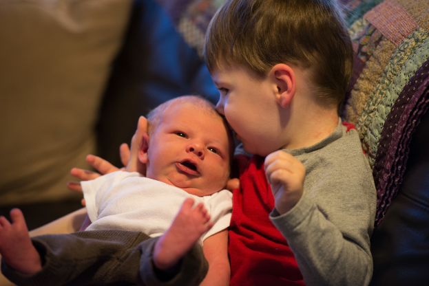 Ein Kind, das ein Baby hält, beide tragen unterschiedliche farbige Kleider, mit einem unscharfen Hintergrund.