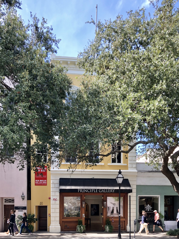Eine Gruppe von Menschen geht an der Principal Gallery in Charleston, SC vorbei, mit Topfpflanzen, einer Straßenlaterne, einem Schild, einer Fahne, einem Flaggenmast und einem bewölkten Himmel.