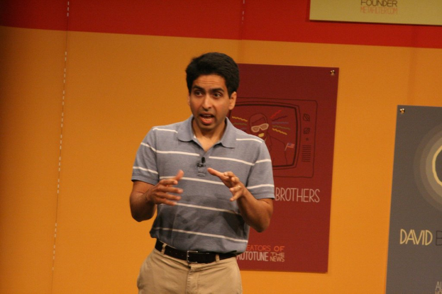 Ein Mann steht auf der Bühne und spricht vor einer Wand mit Postern