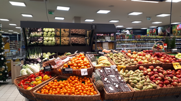 Ein Ladeneinrichtungsbild mit Körbüssern, Gemüsesel, Preisschildern, einem dekorierten Weihnachtsbaum auf der linken Seite und Regalen mit anderen Artikeln im Hintergrund.