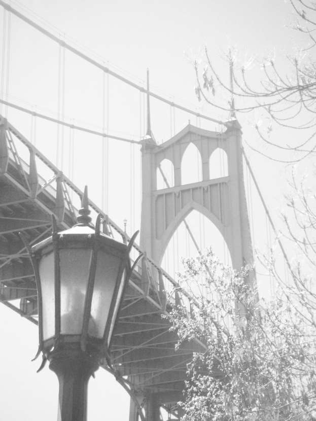 Ein altes Bild einer Hängeseilbrücke mit einem schwarzen Laternenmast vorne unten und einem Baum in der rechten Ecke.