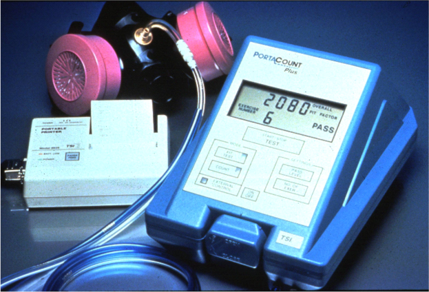 Eine Gasmaskierung wird auf einem Tisch neben einem elektronischen Gasdetektorgerät mit einem angeschlossenen Kabel platziert.