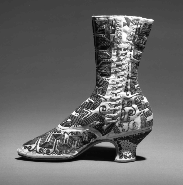 Ein Paar hochhackige Stiefel mit farbenfroher, detallierter Stickerei in einem Schwarz-Weiß-Foto.