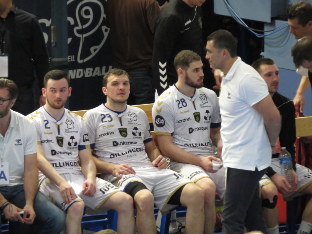 Eine Gruppe von Männern auf einer Bank sitzend, einige halten Flaschen, mit einem Banner im Hintergrund mit der Aufschrift "Nordkraque vs Bordeaux."