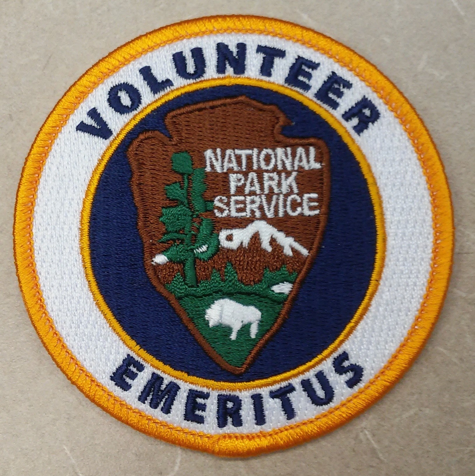 Runder Flicken mit blauem Rand und weißem Hintergrund, mit schwarzer "Volunteer National Park Service Emeritus"-Beschriftung in der Mitte eines gelben Kreises.