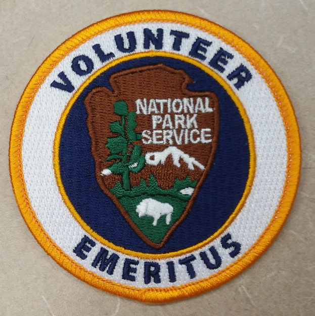 Runder Flicken mit blauem Rand und weißem Hintergrund, mit schwarzer "Volunteer National Park Service Emeritus"-Beschriftung in der Mitte eines gelben Kreises.