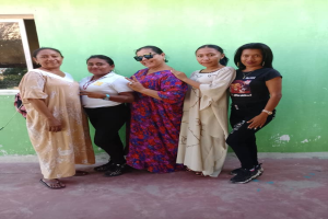 Eine Gruppe von Frauen steht zusammen vor einer grünen Wand mit einem Fenster auf der linken Seite und nimmt an einem Internationalen Frauentag teil.