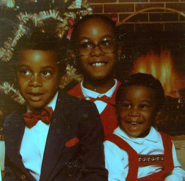 Drei Kinder, die vor einem Weihnachtsbaum mit einem Kamin aus Holz lachen.