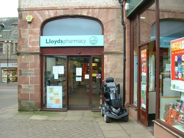 Apothekenladen mit einem Fahrzeug vor dem Gebäude und einem Gebäude in der linken Ecke.