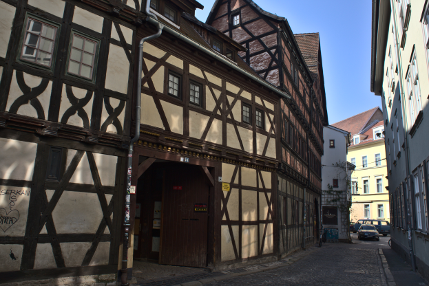 Eine Kopfsteinpflasterstraße in Rothenburg ob der Tauber, Deutschland, gesäumt von Gebäuden auf beiden Seiten unter einem klaren blauen Himmel mit Fahrzeugen, die die Straße entlangfahren.