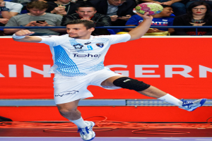 Mann in der Luft mit einem Handball, mit einer Gruppe von Menschen und einem Banner mit Text im Hintergrund.
