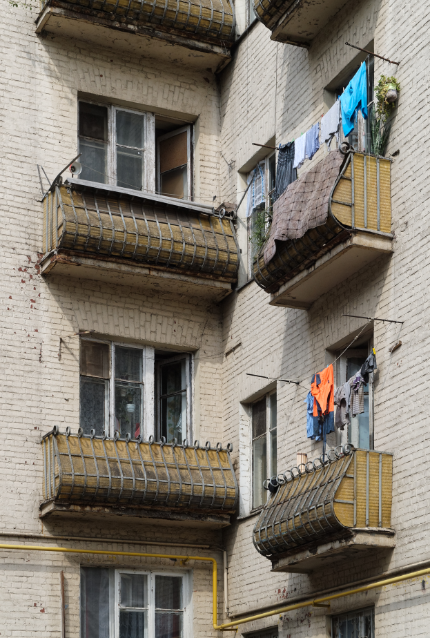 Ein Wohnhaus mit Fenstern, Balkonen, Wäsche, die zum Trocknen hängt, und Rohren an der Seite.