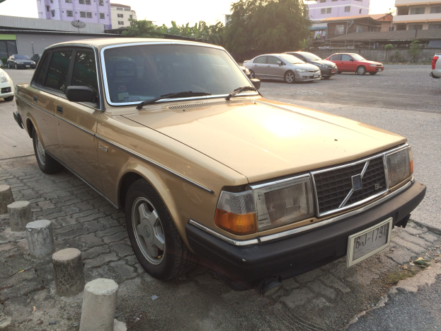 Ein goldener Wagen auf einer Straße mit Gebäuden und Bäumen unter einem klaren blauen Himmel.