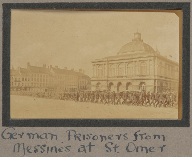 Eine Gruppe deutscher Gefangener aus Messines steht vor einem Gebäude unter einem klaren blauen Himmel, mit Text unten im Bild.