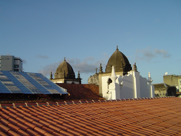 Stadtpanorama mit Gebäuden im Vordergrund und einem blauen Himmel, der Solarpanels auf einem Dach zeigt.