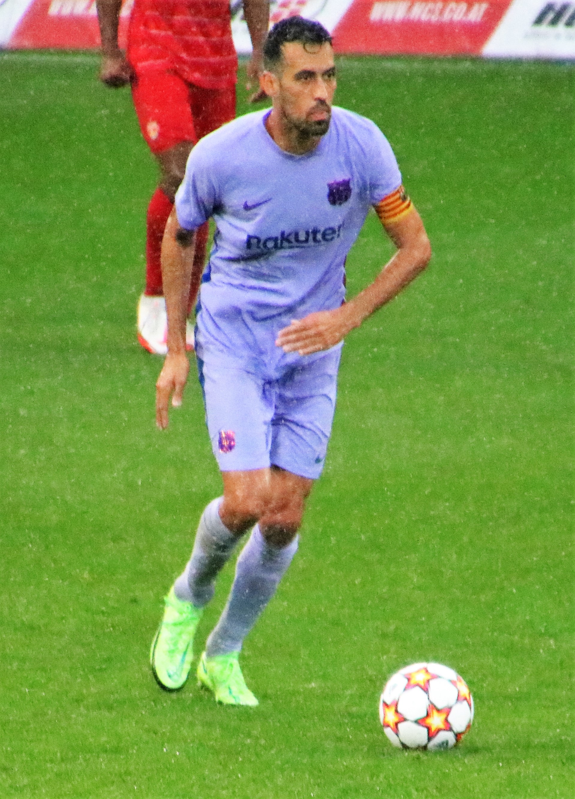 Ein Fussballspieler in einem Sportoutfit und -schuhen ist im Einsatz auf dem Feld, mit einer Tafel mit Text im Hintergrund.