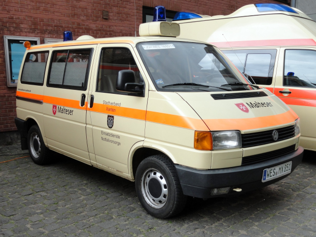 Zwei weiße Rettungswagen nebeneinander vor einem Backsteingebäude mit Fenstern und einer Tür geparkt, unter einem sichtbaren Himmel.