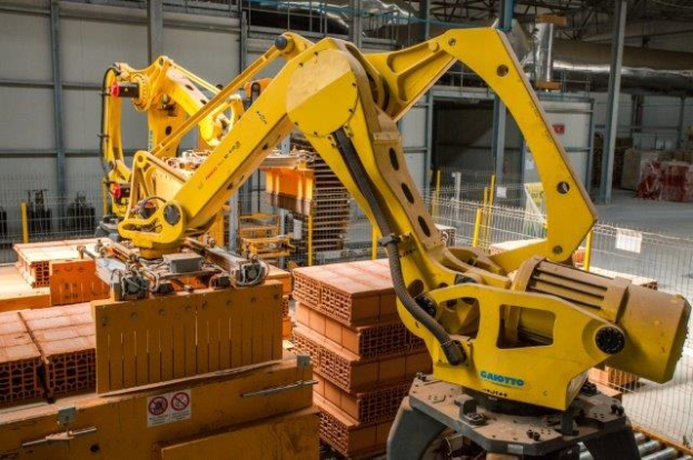 Großes Industriegebäude mit gestapelten Kisten, Überkopfkranen, Zaun, Pfählen und einer fernen Wand in einer Fertigungsumgebung.