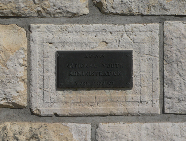 Steinwand mit einem rechteckigen Schild, auf dem "Nationales Jugendamt" in weißer, fetter, zentrierter Schrift auf einem schwarzen Hintergrund steht.