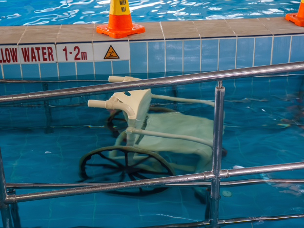 Schwimmbecken mit einem Stuhl in der Mitte, umgeben von Sicherheitskegeln und einem Geländer und einem Schild an der Wand, das die verfügbare Schwimmausrütstätigt.