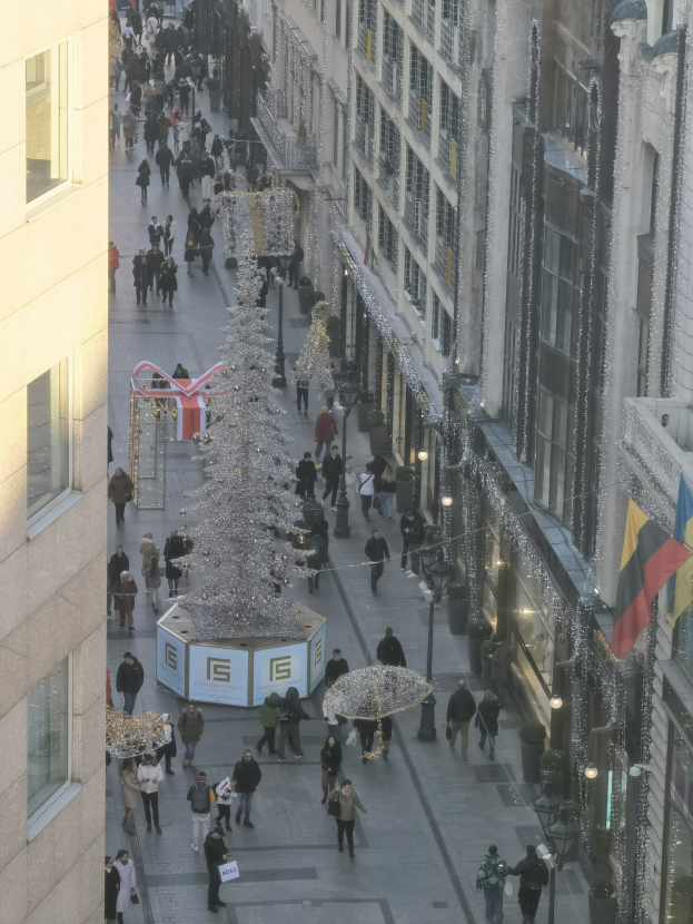 Eine belebte Stadtstraße mit hohen Gebäuden auf beiden Seiten, die einen großen, geschmückten Weihnachtsbaum in der Mitte zeigt.