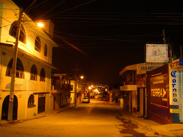 Eine Straßenszene mit Gebäuden und Strommasten auf beiden Seiten, einige geparkte Fahrzeuge vor den Gebäuden und eine Straße in der Mitte.