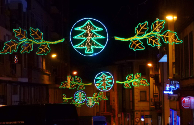 Eine städtische Straße, geschmückt mit festlichen Weihnachtslichtern mit Blättern und anderen Schmuckstücken, mit Fahrzeugen, die an Gebäuden auf beiden Seiten vorbeifahren.