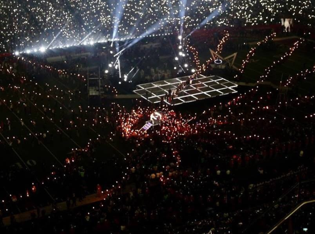 Eine große Menschenmenge in einem hell erleuchteten Stadion bei Nacht mit einem Performer auf der Bühne in der Mitte während der Olympischen Abschlusszeremonie.
