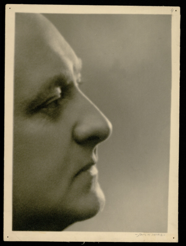 Ein Schwarz-Weiß-Foto eines Mannes mit einem prominenten Nasenrücken vor einem schwarzen Hintergrund.