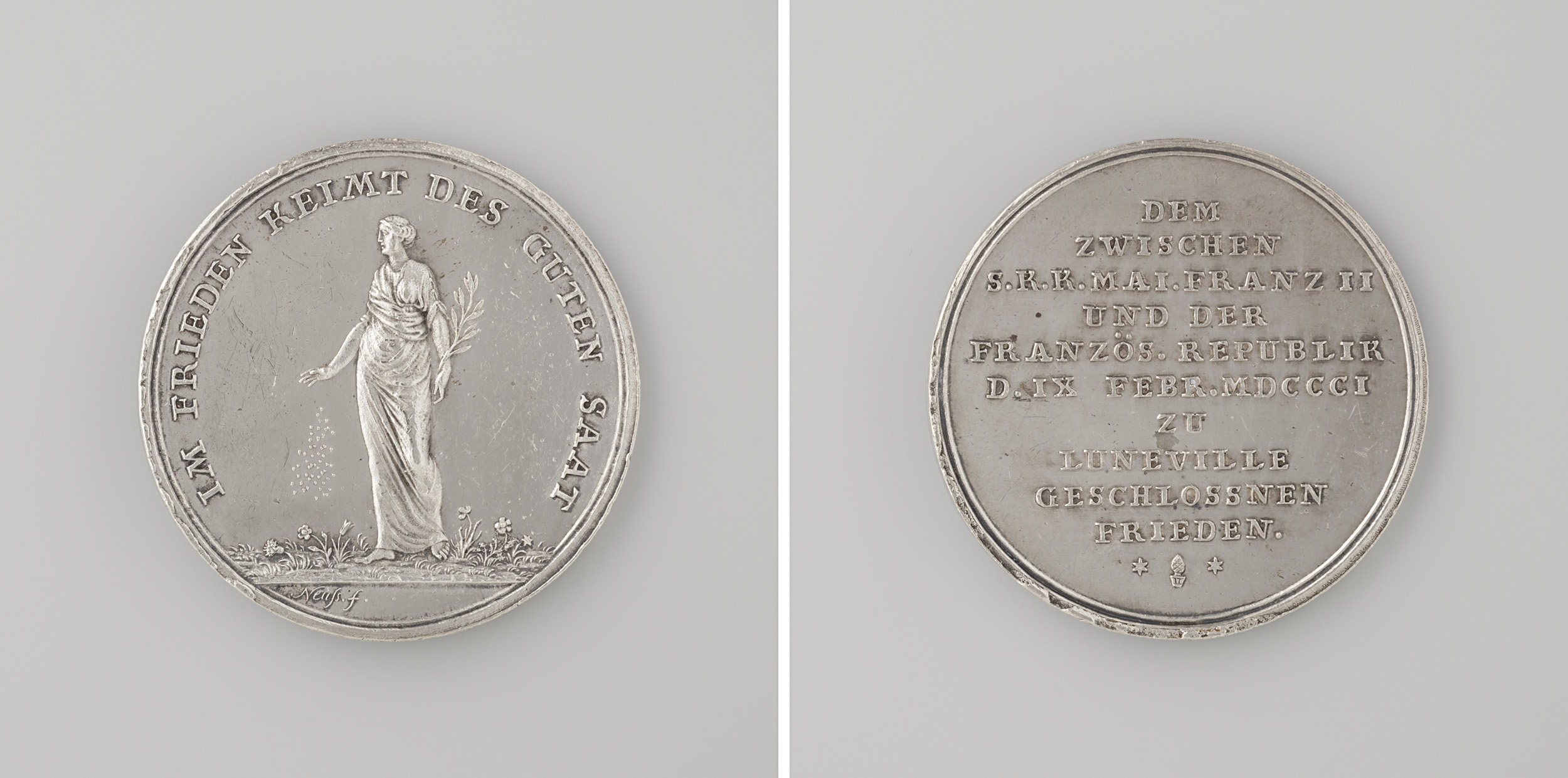 Silberne Medaille mit der Aufschrift 'Medaille' zeigt eine eingravierte Frau mit ausgestreckten Armen und leicht geneigtem Kopf.