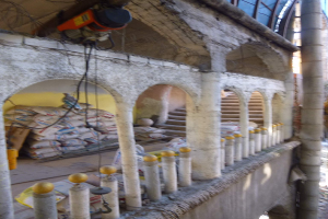 Altes Gebäude mit Bogengängen, Säulen und Treppen wird renoviert, mit verstreuten Werkzeugen, Materialien und Gegenständen, darunter Taschen und eine Maschine mit Drähten oben drauf.