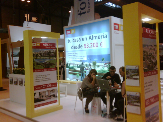 Eine Gruppe von Menschen sitzt um einen Tisch herum und schaut auf einen Laptop, mit mehreren Flyern, auf denen verschiedene Werbeanzeigen zu sehen sind.