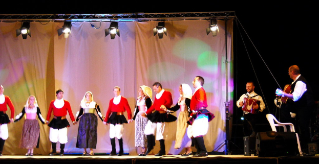 Performer auf der Bühne mit einem Vorhang im Hintergrund, Scheinwerfer oben, Musiker, die Instrumente spielen, auf der rechten Seite und ein weißer Stuhl in der rechten unteren Ecke.