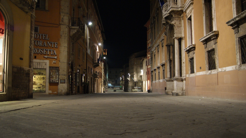 Eine nächtliche Straßenansicht mit Gebäuden auf beiden Seiten und einem Geschäft auf der linken Seite sowie Lichtern in der Mitte.