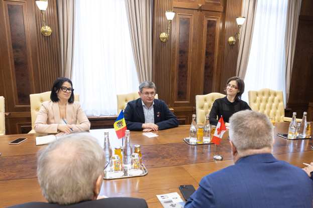 Eine Gruppe von Menschen in einer offiziellen Umgebung an einem Holztisch sitzend mit EU-bezogenen Gegenständen, die in einer Diskussion vertieft sind.
