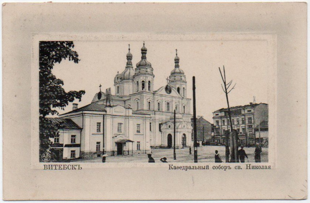 Altes Schwarz-Weiß-Foto einer Kirche umgeben von mehrstöckigen Gebäuden, Strommasten, Passanten und Bäumen, mit aufgedrucktem Text am unteren Rand.