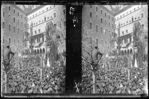 Ein Schwarz-Weiß-Foto einer großen Menschenmenge vor einem Gebäude mit Fenstern, Bäumen und Flaggen im Hintergrund, die scheinbar eine Protestaktion durchführen, wobei einige Schilder und Transparente tragen.