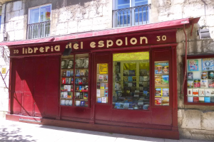 Ein zweistöckiges Gebäude mit Fenstern und Geländern, das einen Ladeneingang mit einer roten Markise zeigt, auf der 'Libreria del Espolon' steht und innen ordentlich aufgereiht Bücher zeigt.