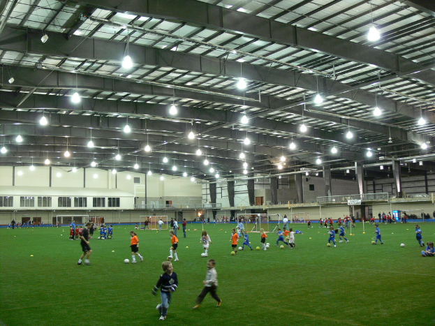 Eine Halle mit Fußballfeld, Spielern, Toren und Deckenbeleuchtung.