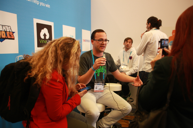 Ein Interview findet statt mit Menschen mit Mikrofonen und einer Kamera, mit Personen im Vordergrund und einem Banner links, während der Hintergrund klar ist.