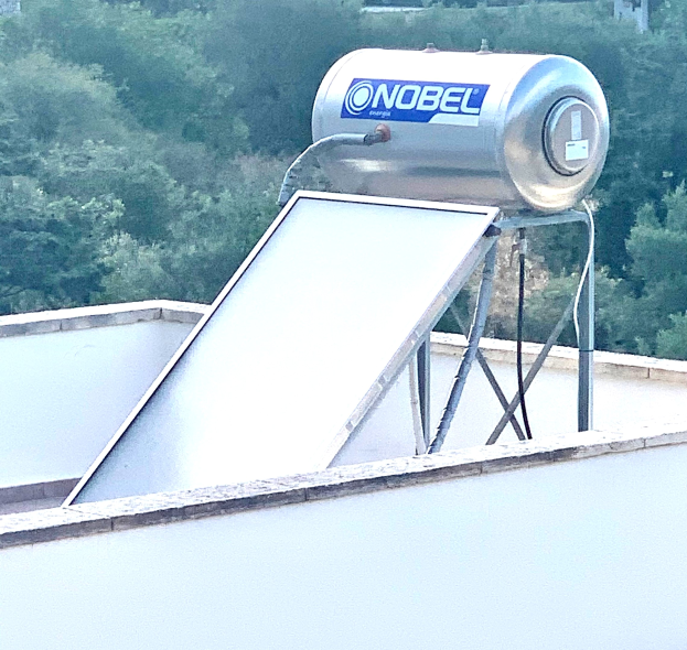 Solarwassererhitzer mit Speicher auf dem Dach eines Gebäudes, Bäume im Hintergrund.